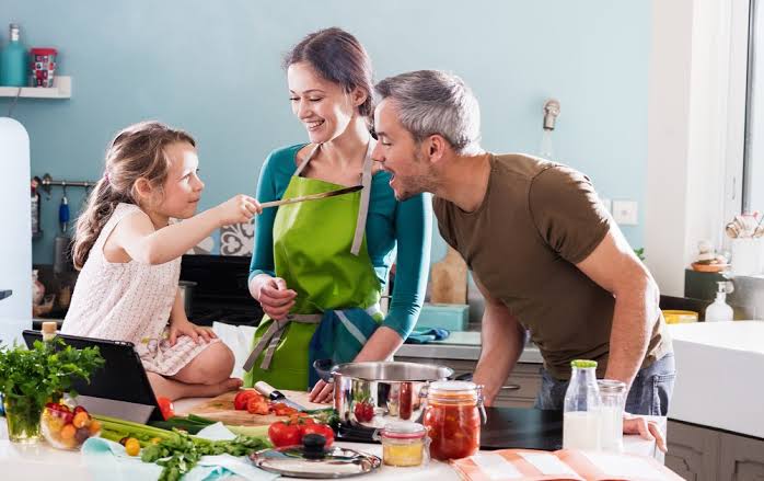 Madre, padre e hija cocinando juntos en la cocina con verduras frescas sobre la mesa