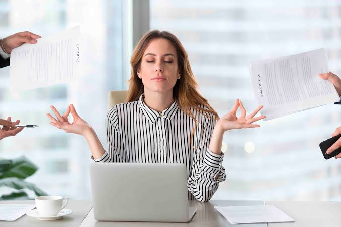 Mujer respirando con calma frente a su computador mientras le entregan documentos por ambos lados